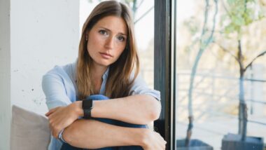 Depressed young woman thinking about breakup sitting by the window alone at home.