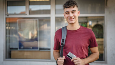 portrait of teenager man stand in front of bank ATM hold credit card