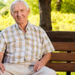 Old man sits on bench. Elderly guy is smiling. He deserves a good rest. All problems left behind.