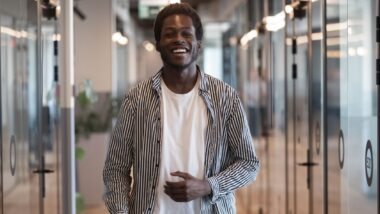 Smiling young black business man professional looking at camera standing in modern office hallway.