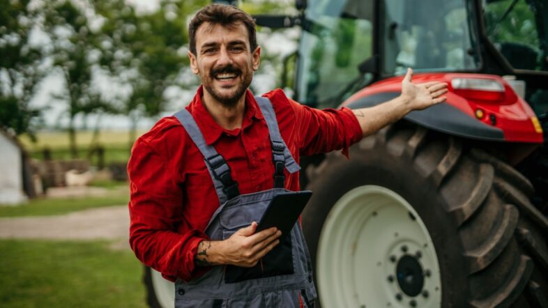 Portrait of a farmer man using a digital tablet and standing next to the tractor. Modern agriculture concept.