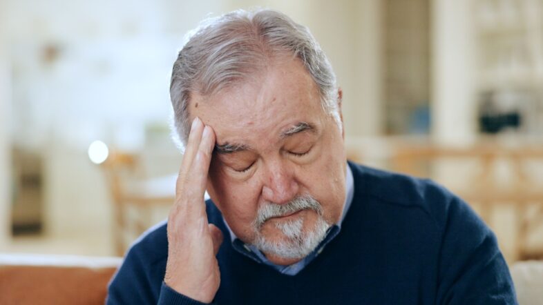 Senior man, headache and stress in mistake, financial crisis or retirement debt on living room sofa at home.