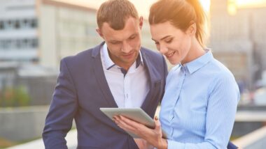 Business couple looking at tablet. Young caucasian people outdoor. How to make money online.